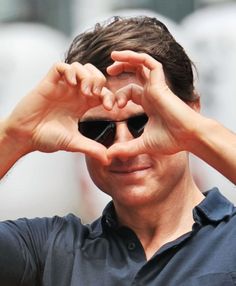 a man making a heart with his hands while holding up the top of his sunglasses