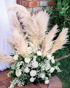 a vase filled with white flowers on top of a brick floor next to a wall