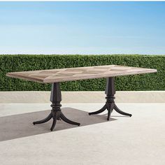 a wooden table sitting on top of a cement floor next to a green hedge covered wall