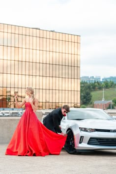 a woman in a red dress standing next to a white car and a man wearing a black suit