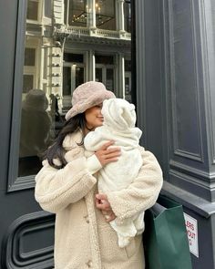 a woman holding a baby in her arms while standing next to a store front window