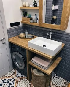 a washer and dryer in a bathroom with grey tiles on the floor, wooden shelves