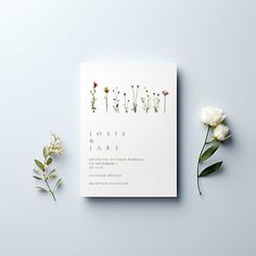 the wedding card is next to flowers and greenery on a gray background with white lettering