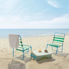 two lawn chairs sitting on top of a sandy beach next to an empty coffee table