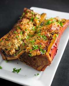 two pieces of meat on a plate with parsley sprinkled on top and another piece of meat in the background