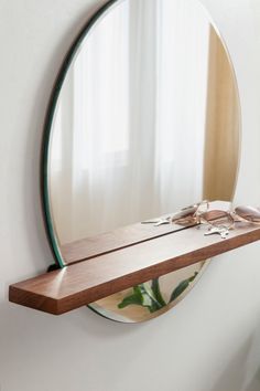 a mirror hanging on the side of a wall next to a shelf with sunglasses and other items