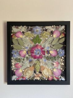 an art work with flowers and leaves on the wall above it is a black frame