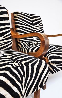 a zebra print upholstered chair with wooden arm rests against a white wall background