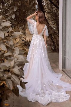 a woman in a white wedding dress is looking out the window at trees and bushes