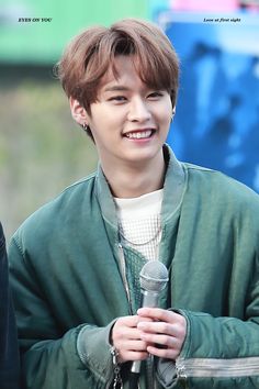 the young man is holding a microphone in his hand and smiling at the camera while wearing a green jacket