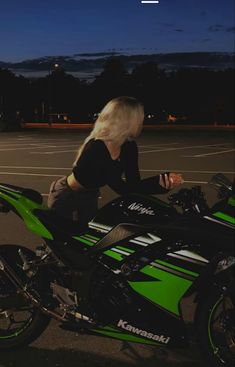 a woman sitting on top of a green and black motor bike in a parking lot