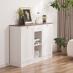 a living room with white furniture and a potted plant on the sideboard next to it