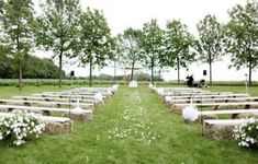 an outdoor ceremony setup with white flowers on the grass and wooden benches lined up in rows