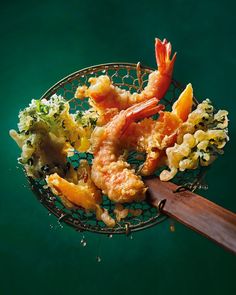 shrimp and broccoli in a wire basket with a wooden spoon on a green surface