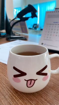 a coffee cup with a face drawn on it sitting on a desk next to a computer