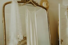 a white bed sitting next to a large mirror on top of a wooden dresser under a hat