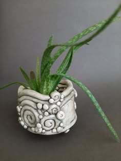 a white ceramic planter with green plants in it on a gray tableclothed surface