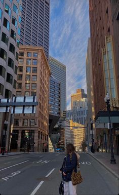 a woman is standing in the middle of an empty street with tall buildings behind her