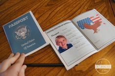 an open passport sitting on top of a wooden table next to a person's hand