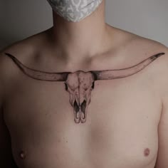 a man with a mask on his face has a bull's skull tattooed on his chest