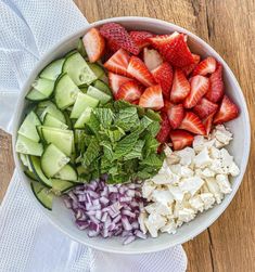 a bowl filled with cucumbers, strawberries, onions and other vegetables on top of a wooden table