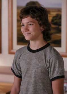 a young boy with curly hair smiling at the camera in front of a painting on the wall