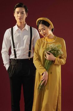 a man and woman standing next to each other in front of a red wall holding flowers