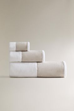 four white towels folded on top of each other in front of a beige wall and floor