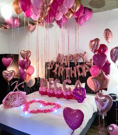 a bed topped with lots of pink and purple balloons