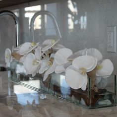 some white flowers are sitting in glass vases on a counter top with water running down the side