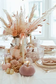 a white table topped with lots of pink and gold plates covered in flowers next to a candle