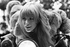 a woman with long hair sitting on top of a motor scooter wearing a fur hat