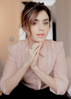 a woman sitting on top of a bed with her hands clasped to her chest and looking at the camera