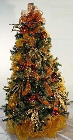 a yellow christmas tree with orange and gold bows on it's top, sitting in front of a white wall