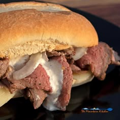 a roast beef sandwich with onions and mayonnaise on a black plate, ready to be eaten