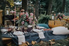 a table set up with flowers and candles for an outdoor dinner party in the woods