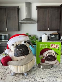 a pug in a santa hat sitting on top of a counter next to a box