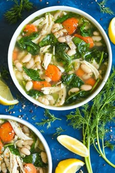 two bowls filled with chicken and white bean soup next to lemons, carrots, and parsley