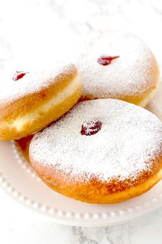 three powdered donuts on a white plate with cranberry filling and powdered sugar