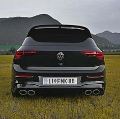 the rear end of a black volkswagen suv parked in a field with mountains in the background