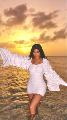 a woman is standing in the water with her arms spread out and wearing a white dress