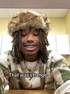 a young man with dreadlocks and a hat on his head is sitting at a table