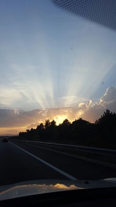 the sun is setting over some trees on the side of the road as seen from inside a car