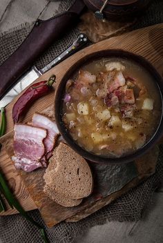 a bowl of soup with meat and bread on a cutting board next to a knife