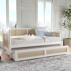 a white day bed sitting on top of a wooden floor next to a large window