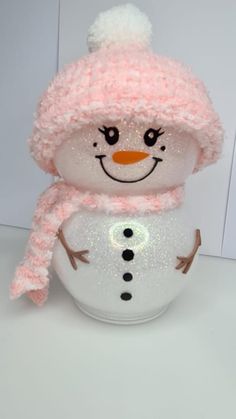 a small snowman with a pink hat and scarf on it's head sitting in a white bowl