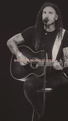 a man with long hair sitting in front of a microphone and playing an acoustic guitar