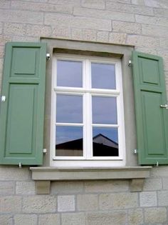 an open window with green shutters on a brick building