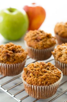 several muffins cooling on a wire rack next to an apple