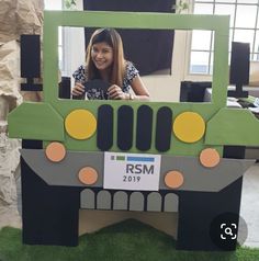 a woman standing in front of a green and black truck shaped cardboard frame with the words rsm on it